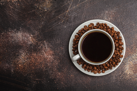 Coffee beans and coffee in a white cup on a dark rusty background. Top view, copy spaceの写真素材