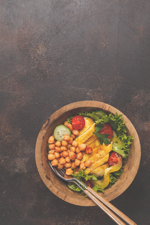 Grilled chicken salad with vegetables and chickpeas in a wooden bowl on a dark background, copy space, top view. Healthy balanced diet concept.の写真素材