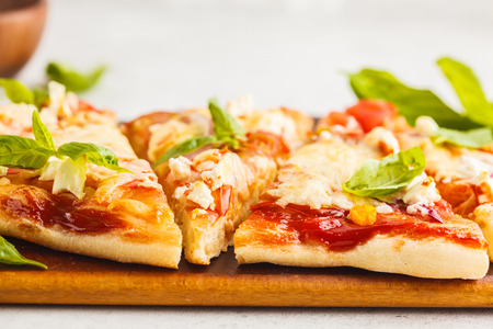 Oval homemade pizza with feta cheese, tomatoes and onions on a wooden board.の写真素材