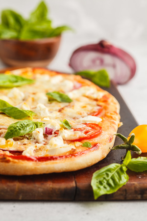 Oval homemade pizza with feta cheese, tomatoes and onions on a wooden board.の写真素材