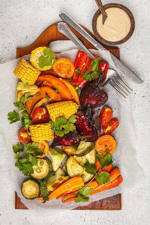 Baked vegetables: pumpkin, beets, carrots, peppers, zucchini and corn on wooden board. White background, top view.の写真素材