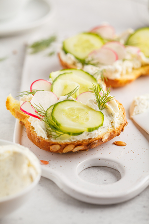 Breakfast cream cheese, cucumber and radish sandwiches on a wooden board. Clean eating food concept.の写真素材