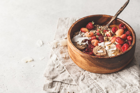 Trendy vegan bowl of oatmeal porridge with berries, raw vegan balls and peanut butter in wooden bowl.の写真素材