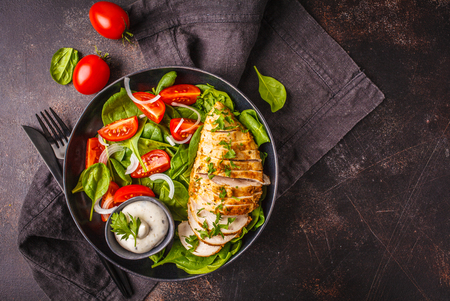 Chicken breast salad with spinach, tomatoes and Caesar dressing, dark background, top view.の写真素材