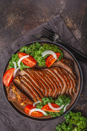 Spicy baked beef with kale salad in a black plate on a dark background, top view, copy space.の写真素材