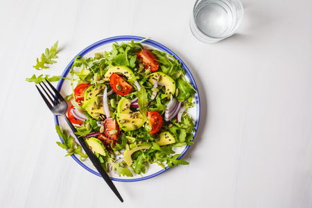 Healthy arugula, avocado, tomatoes salad on white marble background. Plant based diet concept.の写真素材