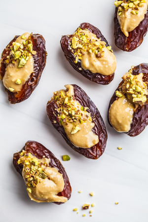 Dates stuffed with peanut butter and pistachios on a white background. Healthy vegan food concept.の写真素材
