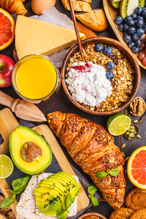 Healthy balanced breakfast on a dark background. Muesli, milk, juice, croissants, cheese, biscuits and fruit, top view.の写真素材