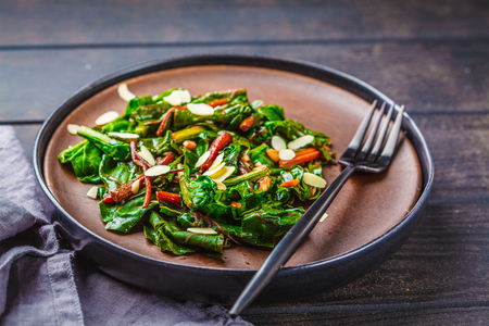 Beet greens salad with nuts in black plate, dark wooden background. Healthy vegan food concept.の写真素材