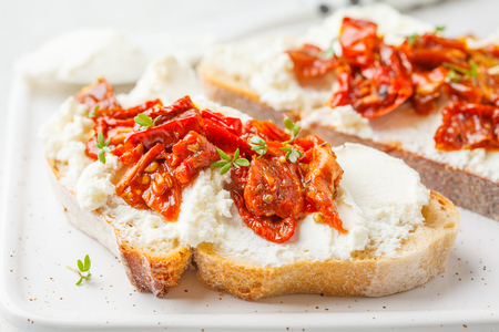 Ricotta and sun dried tomatoes sandwiches on a white board.の写真素材