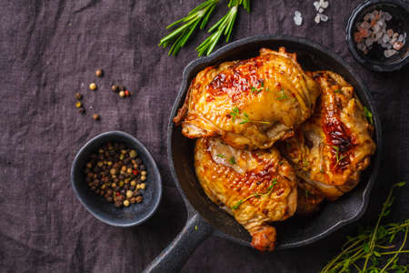 Grilled chicken in cast iron skillet, top view, dark background.