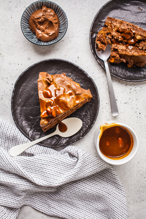 Pieces of homemade snickers cake with chocolate cream and caramel on a black saucer, white background, top view.の写真素材