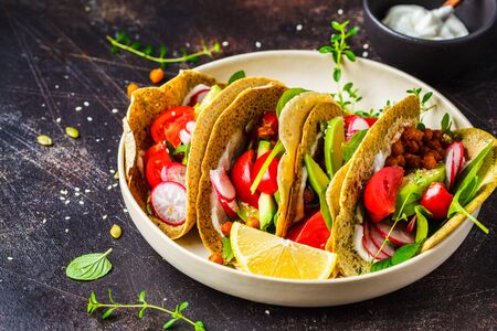 Vegan tacos with baked chickpeas, avocado, sauce and vegetables on a dark background.の写真素材