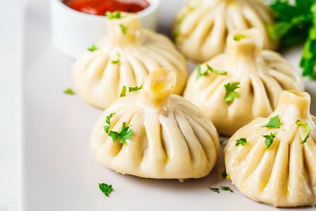Georgian traditional dumplings khinkali with meat filling and greens on a white dish.