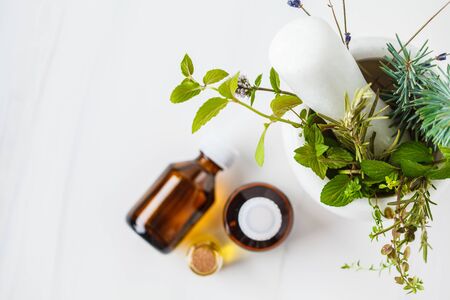 Preparation of essential oil. Different herbs in a mortar and bottles of essential oil, white background.の写真素材