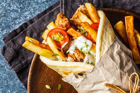 Gyros souvlaki wraps in pita bread with chicken, potatoes and tzatziki sauce, blue background, top...