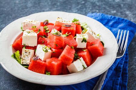 Watermelon salad with feta cheese and herbs in a white plate on a blue background.の写真素材