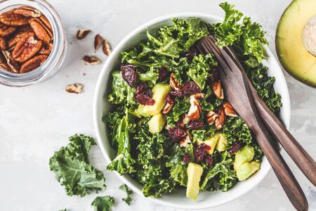 Green kale salad with cranberries and avocado in a white bowl, copy space. Healthy vegan food...