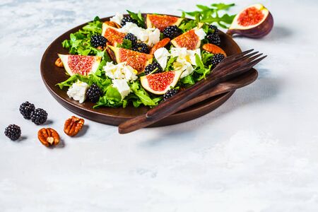 Salad with figs, feta cheese and blackberries in a wooden plate on a white background.の写真素材