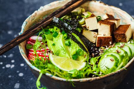Poke bowl with avocado, black rice, smoked tofu, beans, vegetables, sprouts, dark background.の写真素材