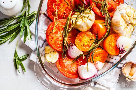 Baked tomatoes with garlic, onions and rosemary in a glass oven dish.の写真素材