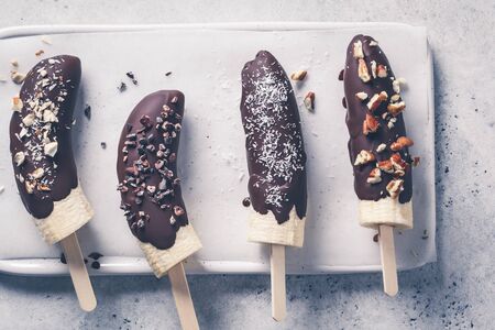 Vegan dessert for kids. Banana in chocolate with nuts, top view.の写真素材