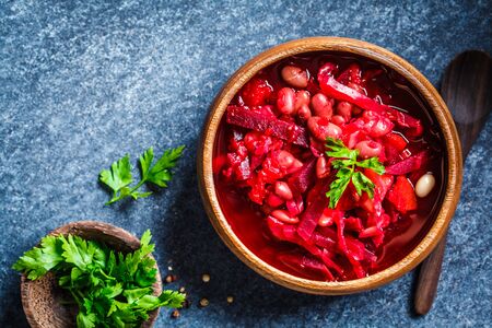Vegetarian beetroot soup borsch with beans in a wooden bowl on a blue background. Healthy vegetarian...