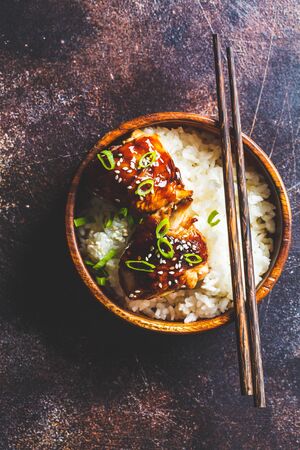 Teriyaki chicken with rice in a wooden bowl, dark background.の写真素材