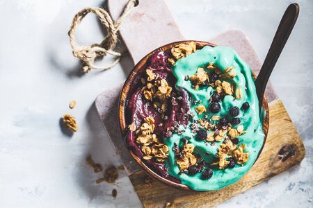 Healthy vegan breakfast. Spirulina and berries smoothie bowl with granola, gray background.の写真素材