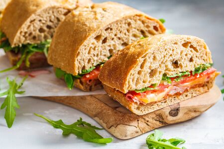 Ciabatta, cheese, ham and vegetable sandwiches on a wooden board.の写真素材
