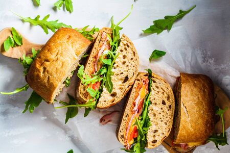 Ciabatta, cheese, ham and vegetable sandwiches on a wooden board.