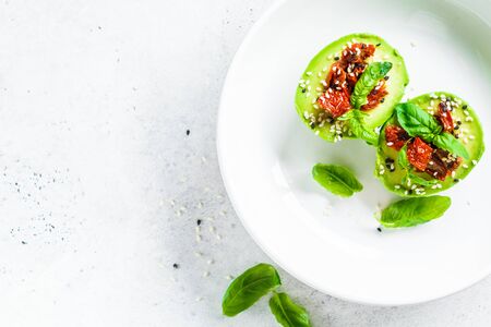 Stuffed avocado halves with sun-dried tomatoes and basil on a white plate, copy space. Healthy vegan food concept.の写真素材