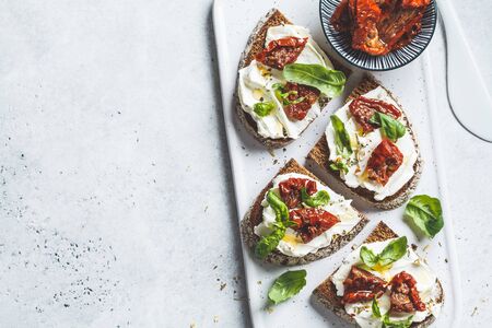 Sandwiches with cottage cheese and sun-dried tomatoes on a white board, copy space.の写真素材