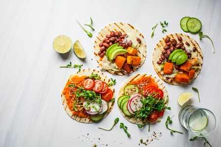 Open vegan tortilla wraps with sweet potato, beans, avocado, tomatoes, pumpkin and seedlings on a white background, top view, flat lay. Healthy vegan food concept.の写真素材