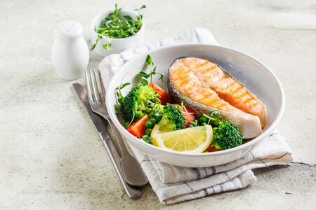 Grilled salmon steak with broccoli and tomatoes in a white plate on a gray background. Diet food concept.の写真素材