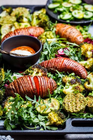 Baked vegetables salad with tahini dressing on cast-iron pan. Baked sweet potato, broccoli and zucchini with arugula. Healthy vegan food concept.の写真素材
