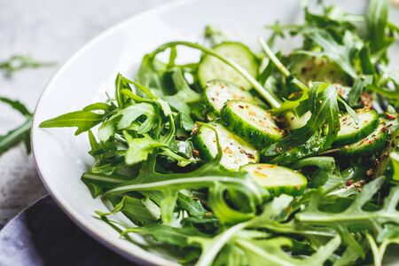 Green salad of arugula and cucumbers with oil and spices in a big gray dish.の写真素材
