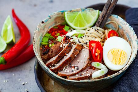 Asian spicy ramen noodles with pork, egg and vegetables in a blue bowl, gray background.の写真素材