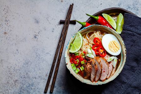 Asian spicy ramen noodles with pork, egg and vegetables in a blue bowl, gray background.の写真素材