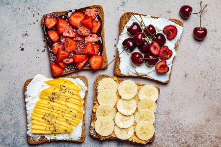Different sweet fruit toasts with banana, mango, cherry and strawberries on a dark background.