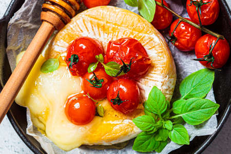 Baked Camembert or Brie cheese with tomatoes in a black pan.の写真素材