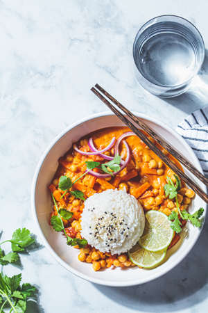 Vegan chickpea curry with rice and cilantro in a white bowl, white marble background. Indian cuisine concept.の写真素材