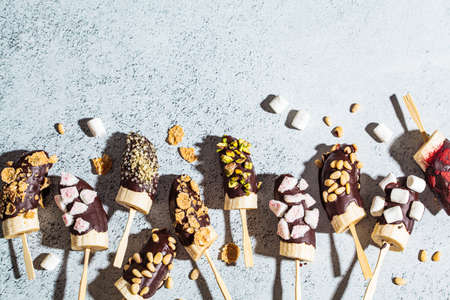 Bananas in dark chocolate with different toppings on a stick, gray background. Healthy vegan dessert...