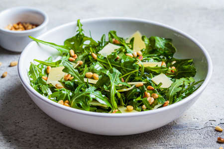 Arugula and parmesan salad with pine nuts in a white bowl. Italian cuisine concept.の写真素材