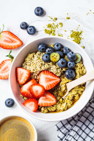 Matcha oatmeal bowl with berries and maple syrup on a white marble background. Healthy breakfast, vegan food, detox recipe.の写真素材