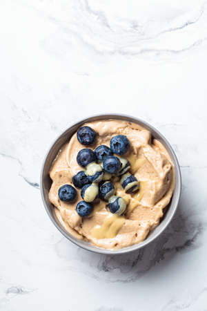 Banana dairy-free ice cream or vegan smoothie bowl with berries and peanut butter, white marble table.の写真素材