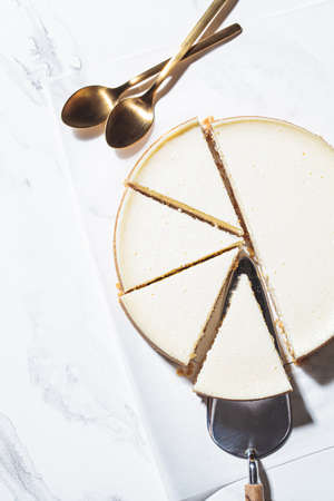 Traditional whole sliced cheesecake on a white marble background.