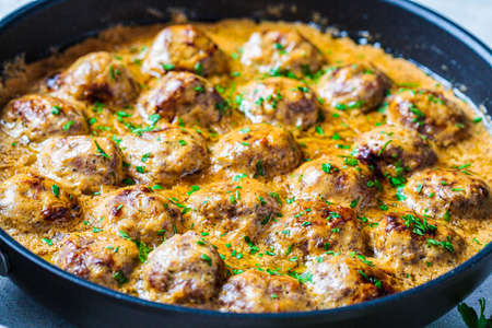 Swedish meatballs in a creamy sauce in a black frying pan, gray background, close-up. Scandinavian food concept.の写真素材