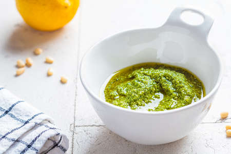 Homemade pesto sauce in a white bowl. Green basil dressing, gray tiles background.の写真素材