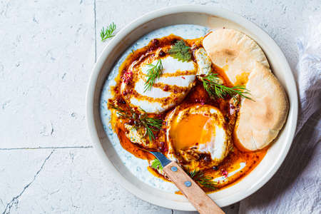 Turkish eggs cilbir in a white bowl. Turkish cuisine concept. Poached eggs with yogurt and spicy butter sauce, top view.の写真素材